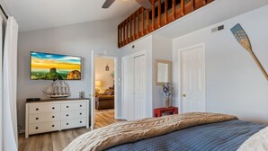A bedroom with a bed, a dresser, a TV, and a wooden staircase.