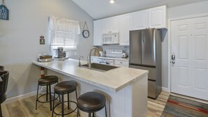 A modern kitchen with white cabinets, a stainless steel refrigerator, a sink, and a bar area with stools.