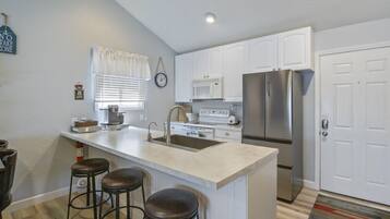 Cocina moderna con armarios blancos, refrigerador de acero inoxidable, lavamanos y un área de bar con taburetes.