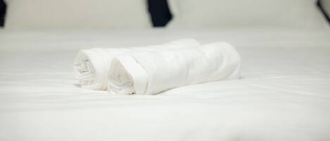 A neatly made bed with a white towel and a dark headboard.