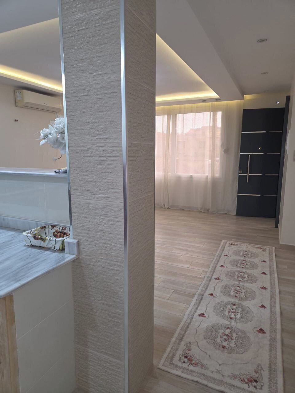 Ein zeitgemäßes Interieur mit hellem Bodenbelag, einem gemusterten Teppich und einer Tür mit schwarzem Einsatz.