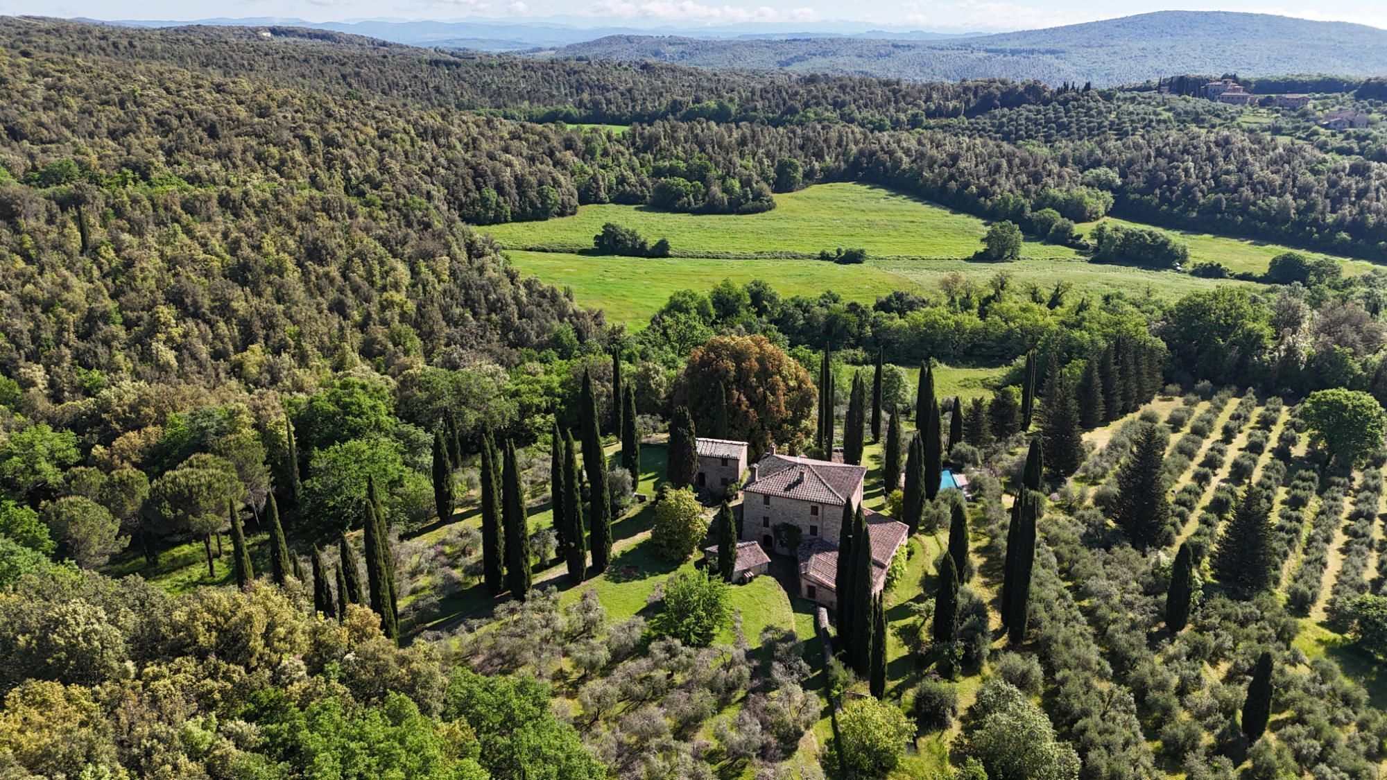 Ländliche Landschaft mit einem Steinhaus, umgeben von hohen Zypressen und offenen Feldern.