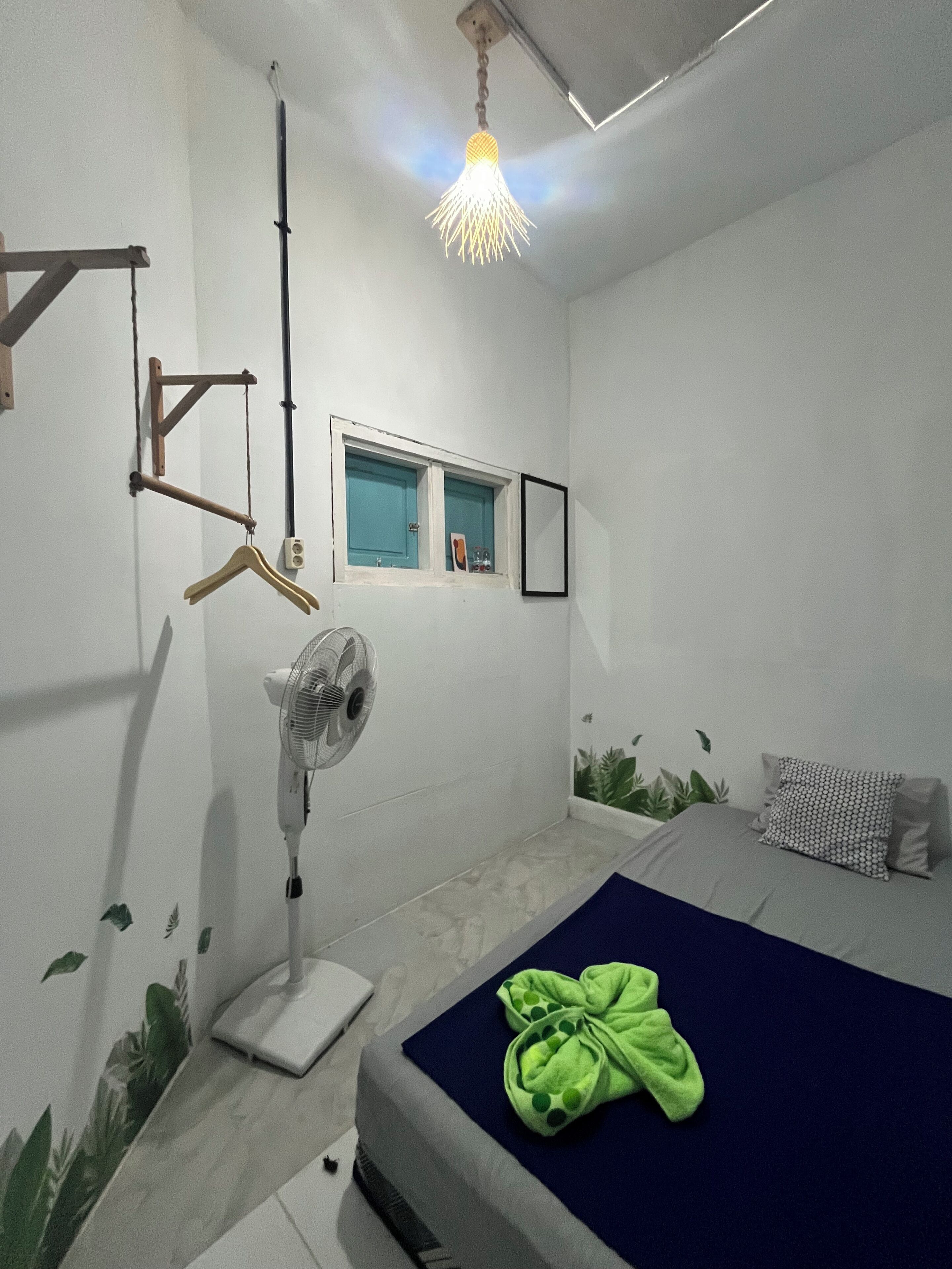 Un dormitorio con cama, ventilador, ventana y lámpara colgante.