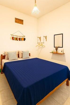 Un dormitorio con cama, lámpara colgante, espejo en la pared y repisa con objetos.