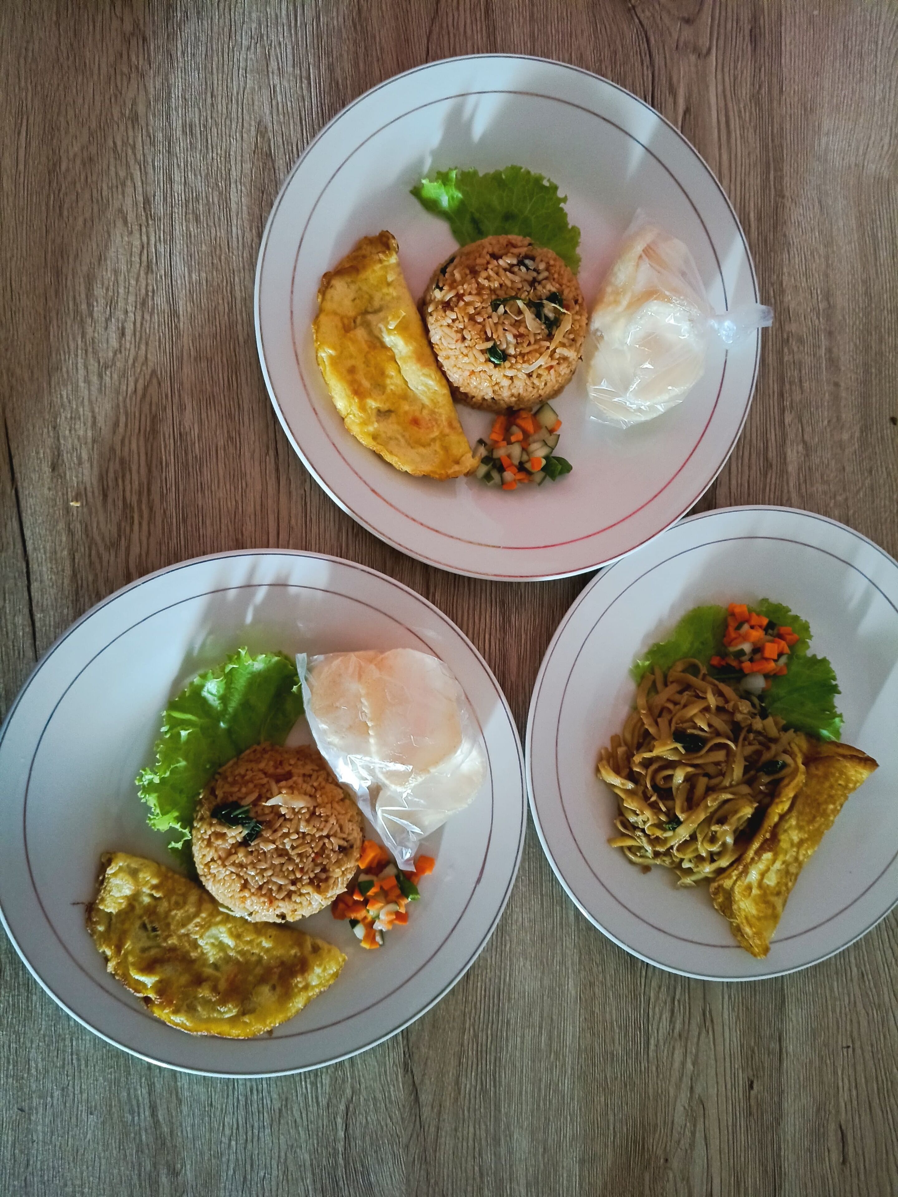 Tres platos de comida con arroz, verduras y un alimento frito, sobre una mesa de madera.