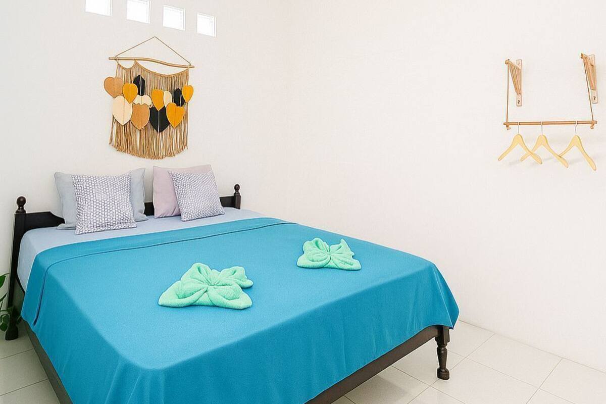 A bedroom with a bed, a hanging light fixture, a wall-mounted decoration, and a clothing rack.