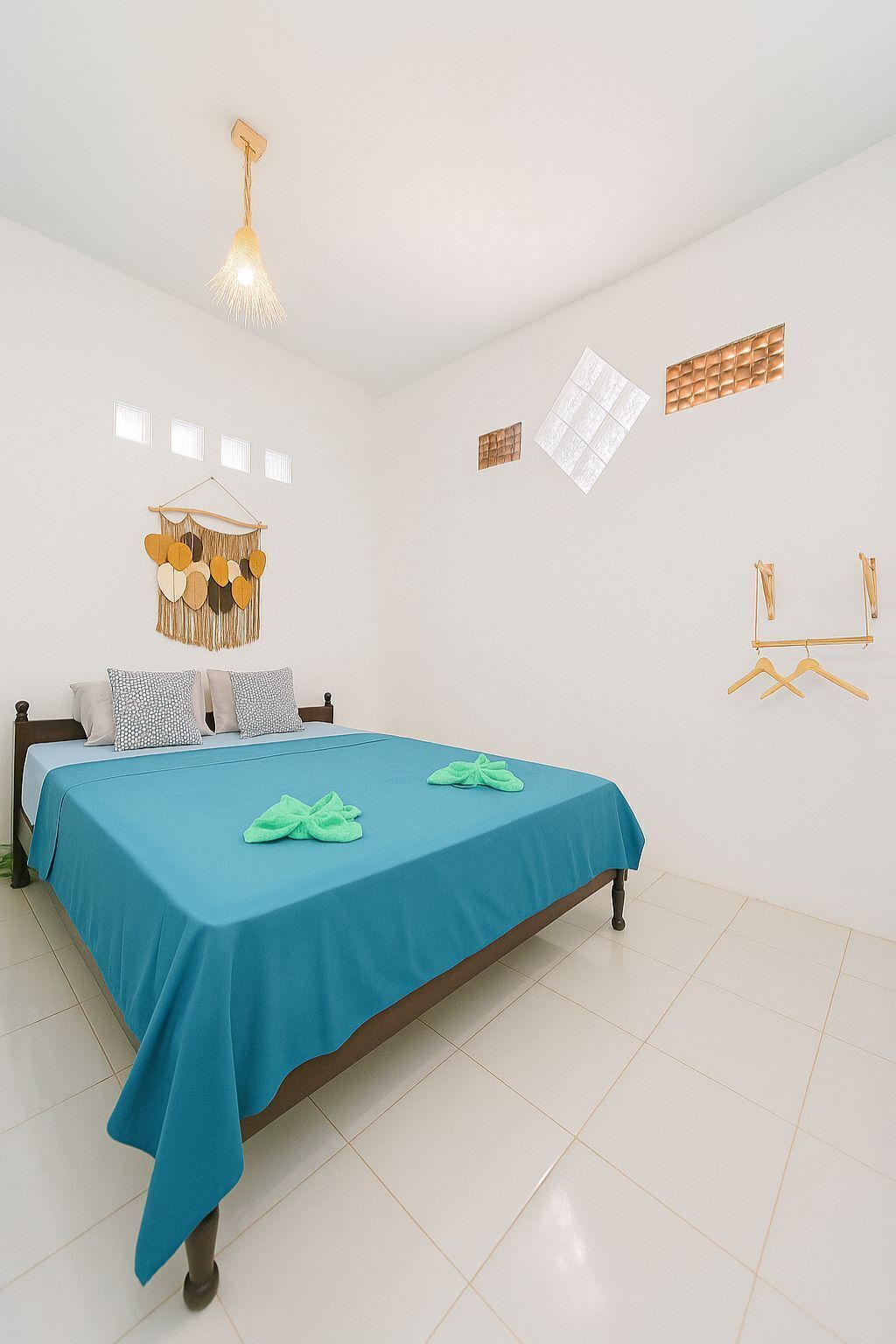 A bedroom with a bed, a hanging light fixture, wall-mounted shelves, and a wall-mounted rack.