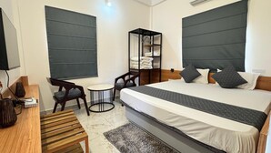 A modern hotel room with a large bed, a small desk, a chair, a round table, and a wardrobe. - Hotel Insta 18 (Siliguri)