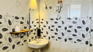 A bathroom with a white sink, a mirror, and a shower with a handheld dryer. - Hotel Insta 18 (Siliguri)