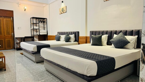 A hotel room with two beds, a wooden wardrobe, a coat rack, and a wall-mounted light fixture. - Hotel Insta 18 (Siliguri)