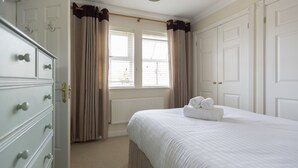 A bedroom with a large bed, a dresser, and a window with curtains. - Castle Mill View, sleeps 4. (Central Oxford)