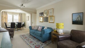 A living room with a blue sofa, brown leather armchair, and a dining area with a table and chairs. - Castle Mill View, sleeps 4. (Central Oxford)