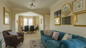A living room with a brown leather sofa, a blue velvet sofa, a floral rug, and a dining area with a table and chairs. - Castle Mill View, sleeps 4. (Central Oxford)