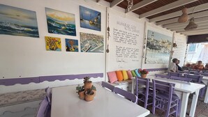 A restaurant interior with white tables and purple chairs, decorated with coastal paintings and a wall with text. - Adahan Otel Bozcaada (Bozcaada)