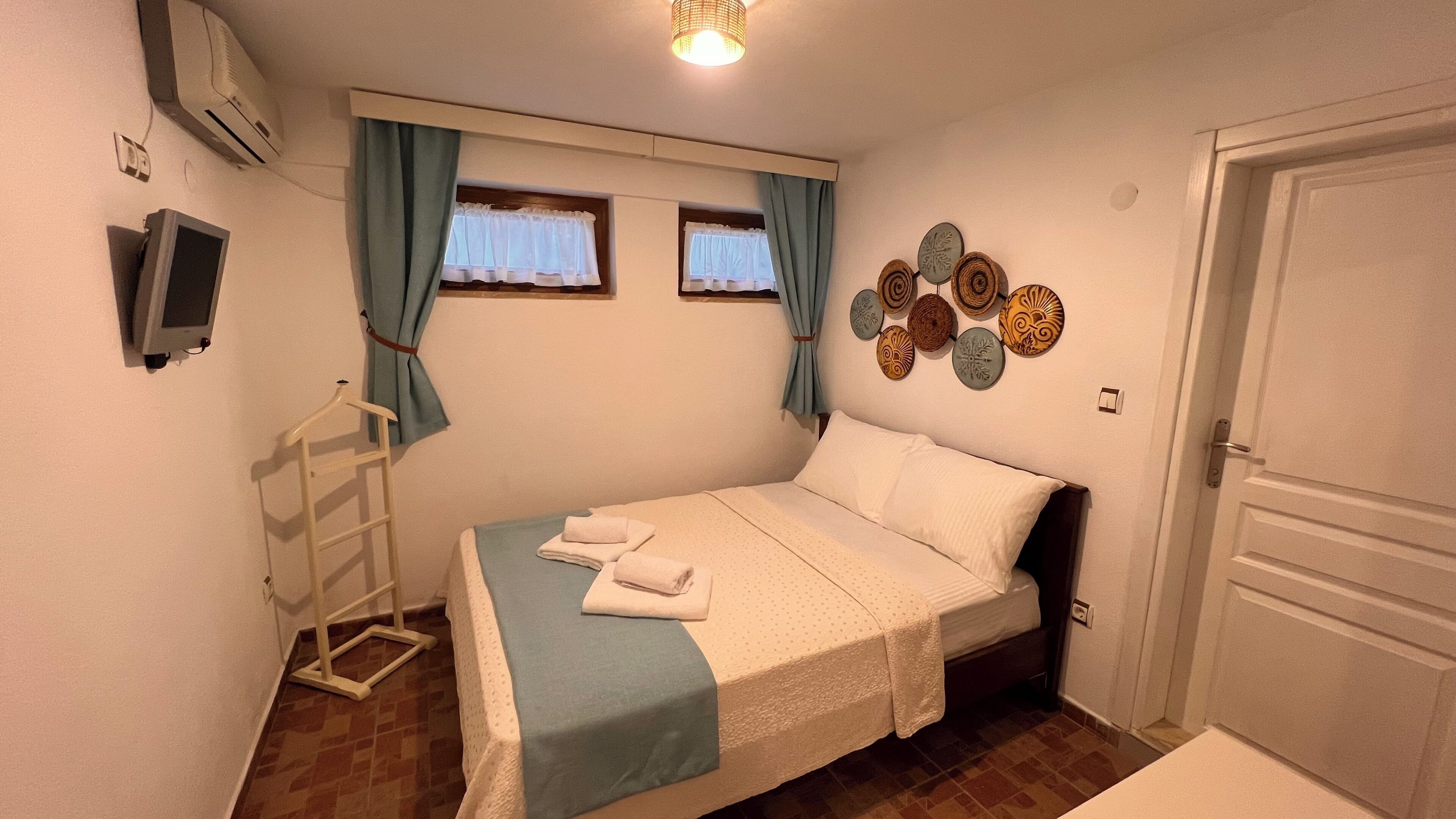 Un dormitorio con cama, televisión, ventana con cortinas, decoración en la pared y una puerta.