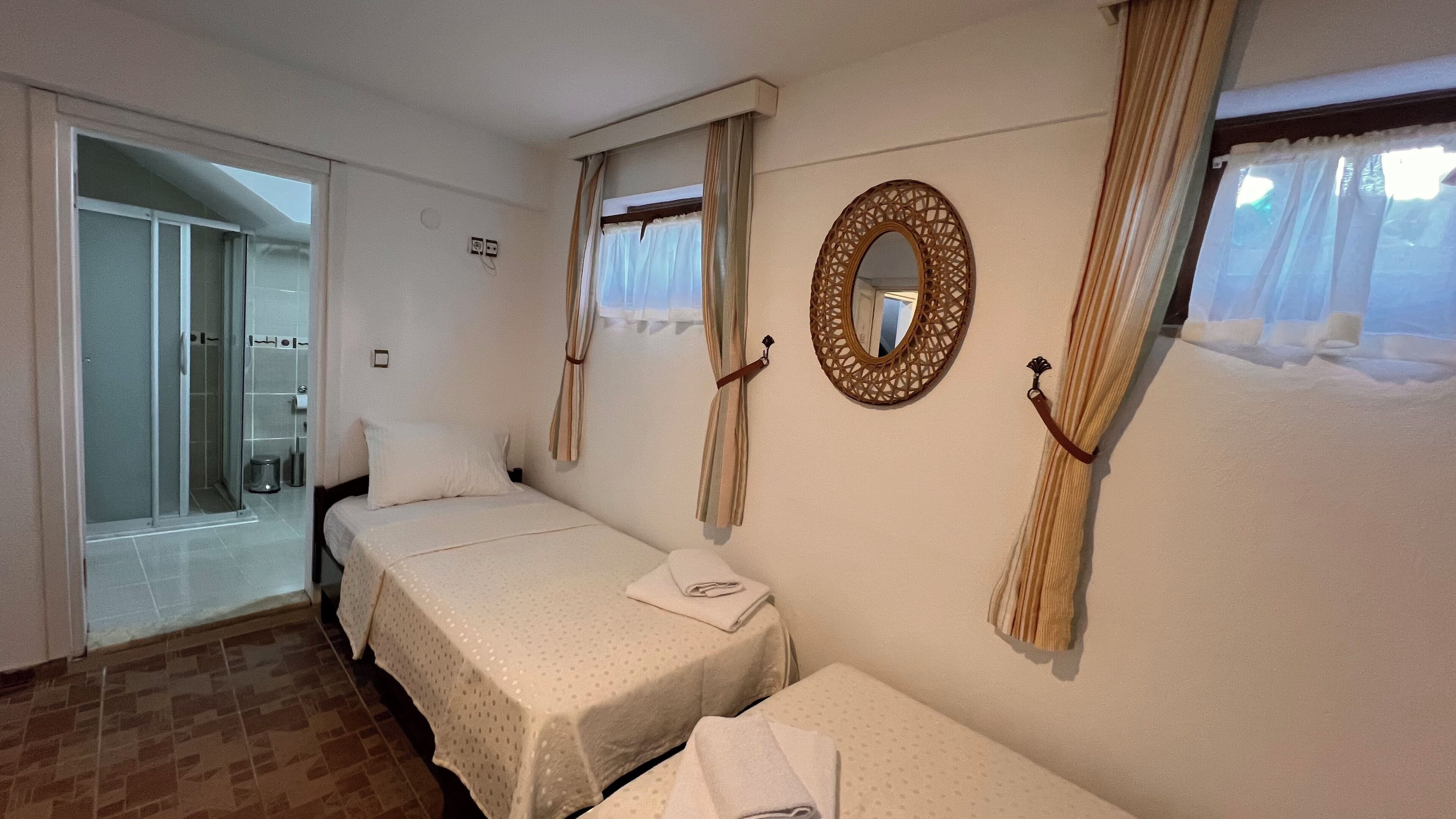 A hotel room with two beds, a shower, and a large mirror on the wall.