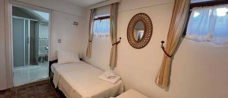 A hotel room with two beds, a shower, and a large mirror on the wall.