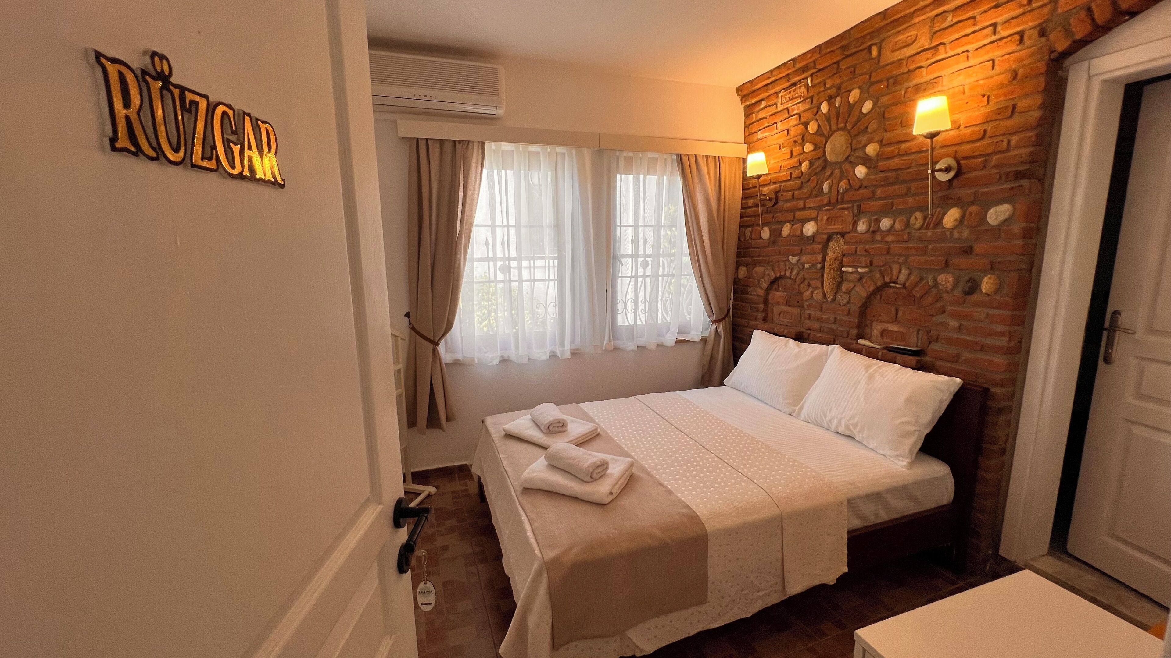 A hotel room with a bed, a brick wall, and a sign that reads "RÜZGAR".