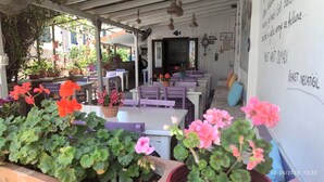 An outdoor cafe with tables and chairs, surrounded by potted plants and flowers. - Adahan Otel Bozcaada (Bozcaada)