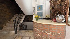 A staircase with a stone wall on one side and a brick wall on the other, leading to a landing with a white door and a clock. - Adahan Otel Bozcaada (Bozcaada)