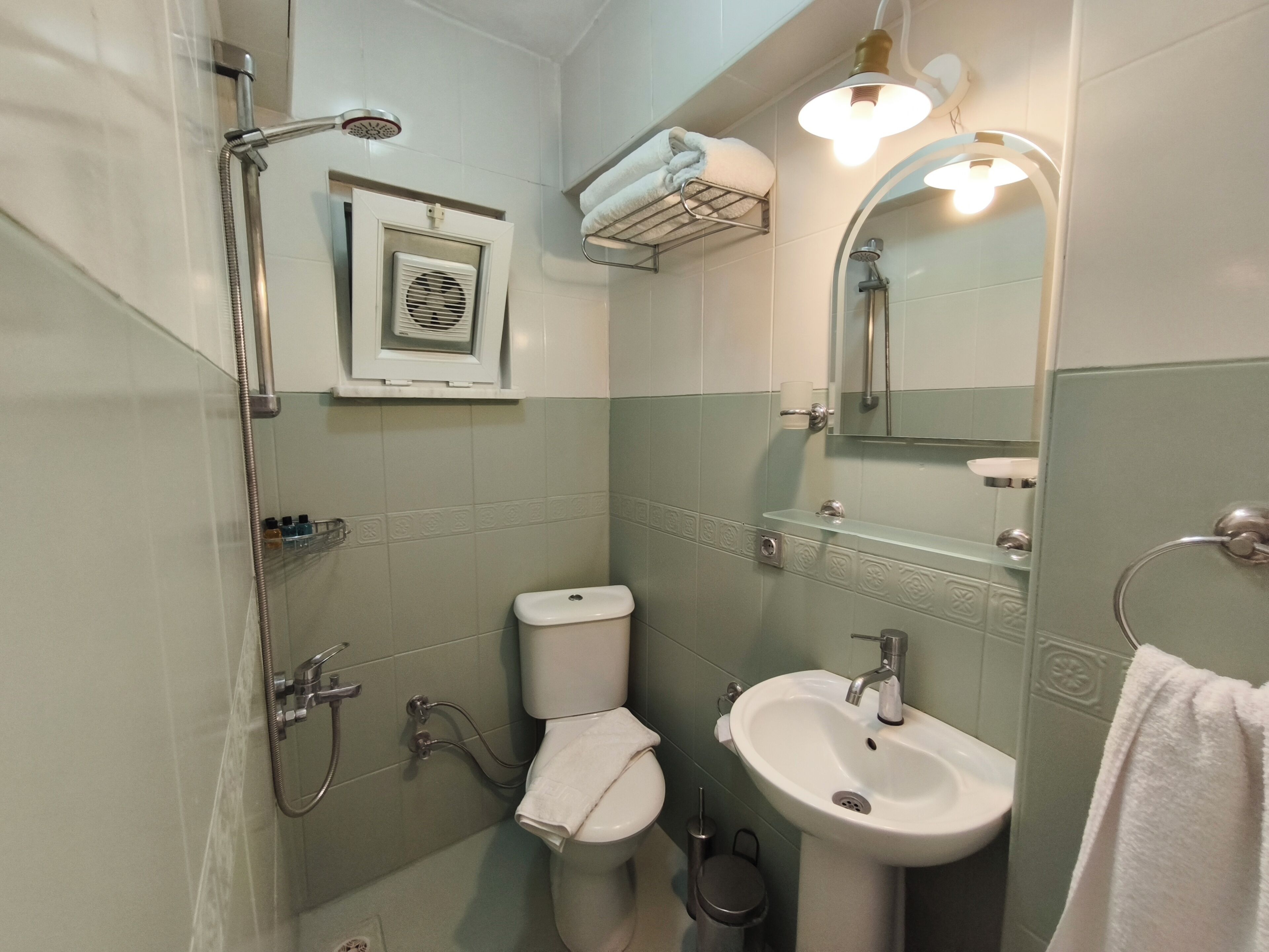 A bathroom with a shower, toilet, sink, and a mirror with lights.