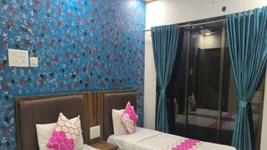 Una habitación con dos camas, cada una con colcha estampada en rosa y blanco, pared con diseño azul y ventana con cortinas color turquesa.