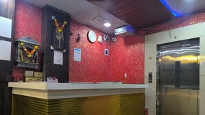 Zona de recepción con pared texturizada de color rojo, un mostrador blanco, un reloj y un ascensor.