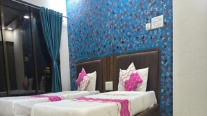 Habitación de hotel con dos camas, cada una con estructura de madera y ropa de cama blanca. La habitación tiene una pared con diseño azul y una ventana con cortinas.