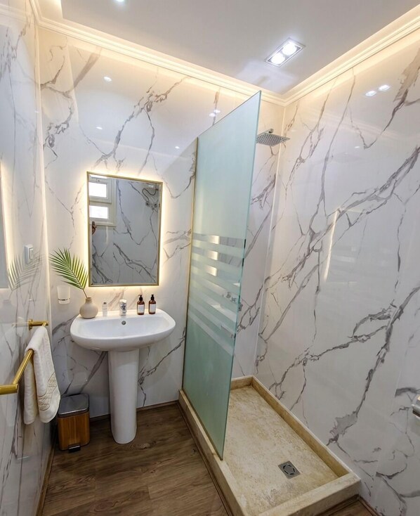 A bathroom with a marble wall, a pedestal sink, a glass shower enclosure, and a wooden floor. - porto view hurghada (Hurghada)