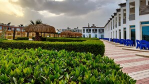 Un hotel con un vialetto lastricato, edifici a tetto di paglia e vegetazione curata.