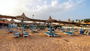Una spiaggia con lettini e ombrelloni, cielo sereno e palme sullo sfondo.