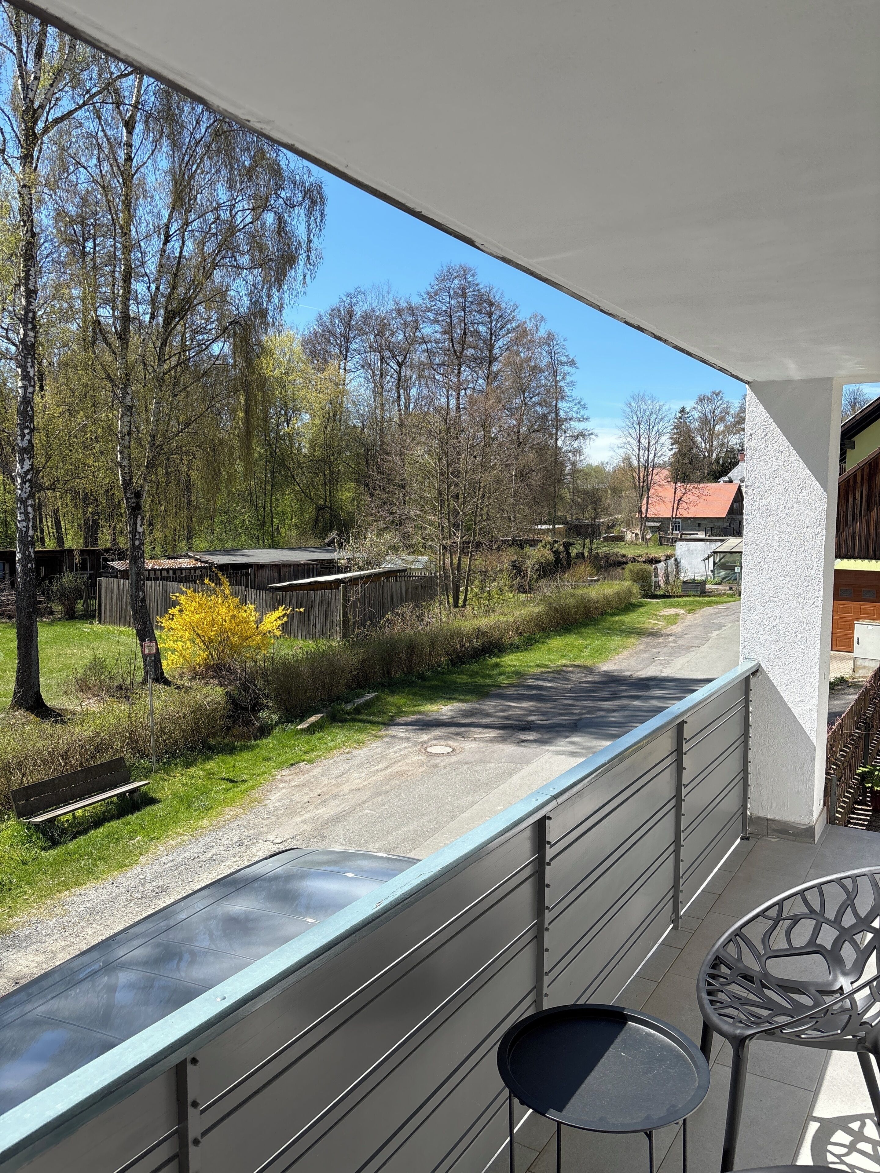 A balcony with a view of a road, trees, and a building in the background.