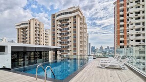 Un área de piscina en la azotea con sillones reclinables y vistas del horizonte de la ciudad.