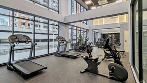 Un gimnasio con cintas de correr, bicicletas estáticas y máquinas de pesas, amplias ventanas y un letrero que dice 'FITNESS CENTER'.