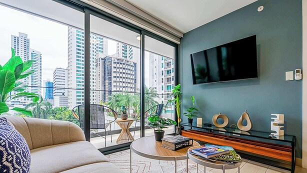 Un salón moderno con un amplio ventanal, un televisor de pantalla plana y un balcón con plantas.