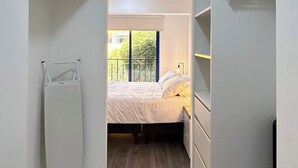 Un vestidor estrecho con cama al final, piso de madera y ventana con vistas a la vegetación.