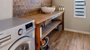 A laundry area with a washing machine, a sink with a vessel basin, and a wooden bench. - Private 3BR Villa with pool (Moorea-Maiao)