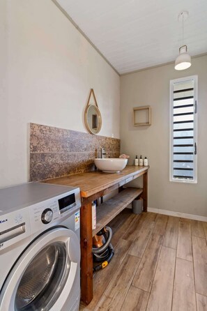 A laundry area with a washing machine, a sink with a vessel basin, and a wooden bench.