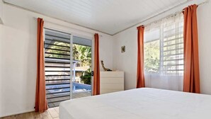 A bedroom with a bed, a dresser, a giraffe statue, and a sliding glass door leading to a balcony. - Private 3BR Villa with pool (Moorea-Maiao)