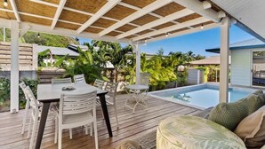 A covered outdoor area with a pool, wooden deck, white furniture, and lush greenery. - Private 3BR Villa with pool (Moorea-Maiao)