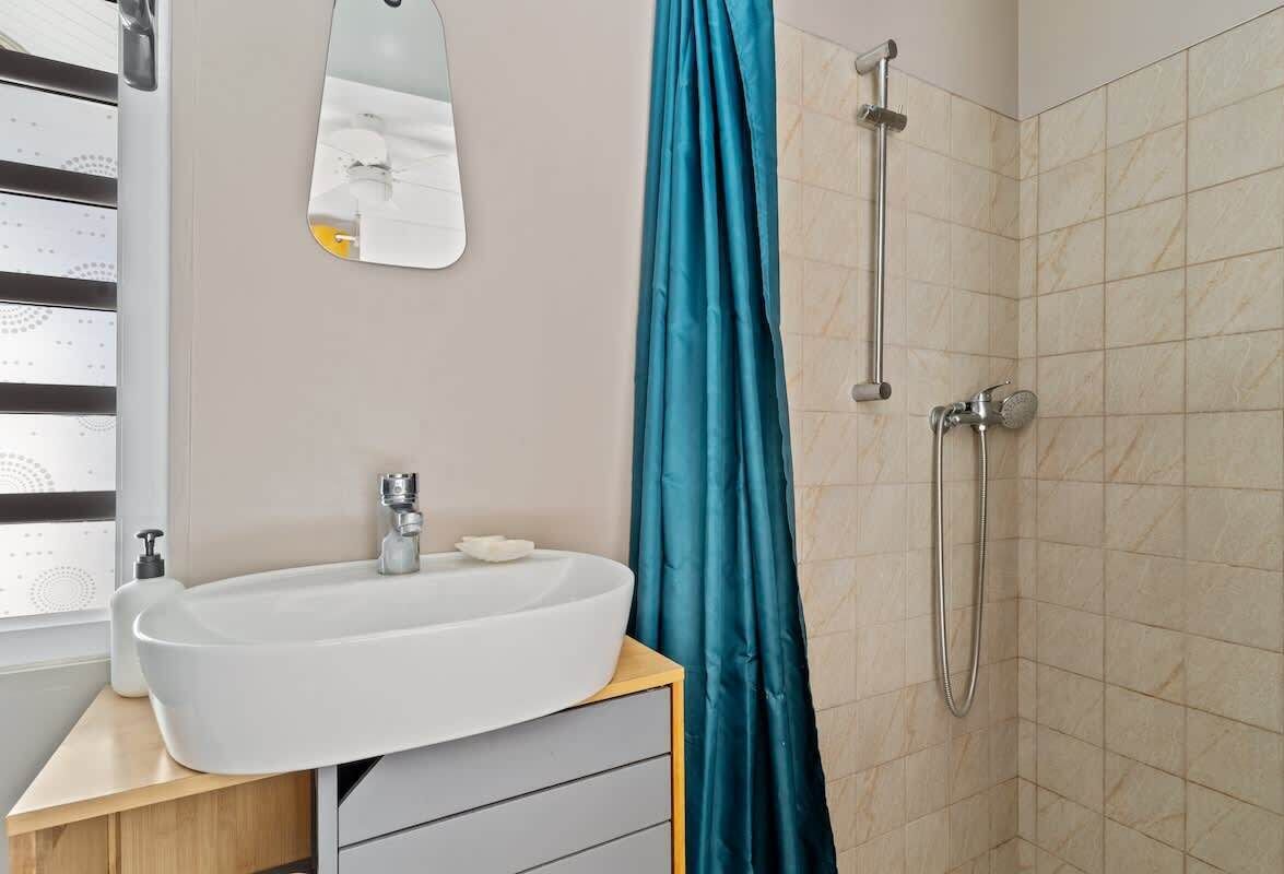 A bathroom with a white sink, a mirror, a shower, and a teal shower curtain.