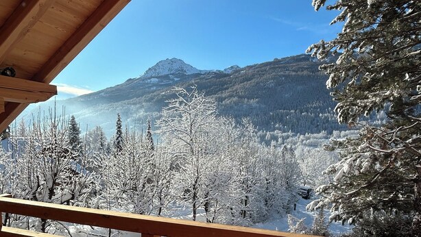 Un balcón de madera con vistas a árboles cubiertos de nieve y una montaña al fondo.