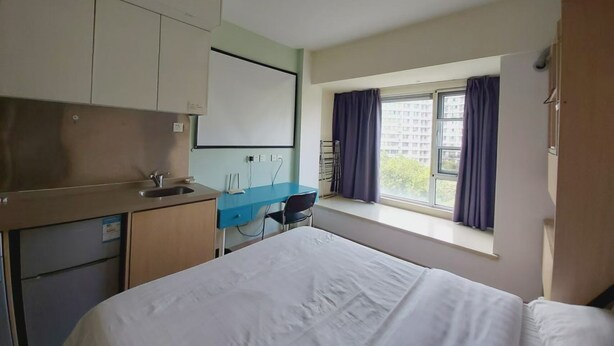 Une chambre d’hôtel avec un lit, une petite kitchenette, un bureau et une fenêtre avec des rideaux.