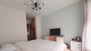 Une chambre d’hôtel avec un grand lit, un téléviseur posé sur un meuble, une petite kitchenette et une porte donnant sur une salle de bain.