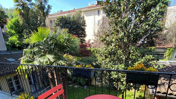 A red metal table and chairs on a balcony with a view of a garden and buildings.