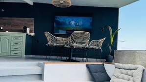 A modern outdoor seating area with a sofa, two wicker chairs, and a coffee table. A television is mounted on the wall, and there is a staircase leading to an upper level. - Luxury Nest with Panoramic Wiews 10 min from Loro Park (Los Realejos)