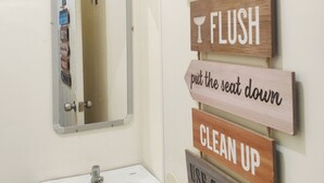 Un baño con lavamanos, espejo y una pared con letreros de madera que indican las normas del baño.