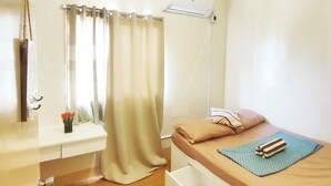 Una habitación pequeña y bien iluminada con cama, escritorio, silla y ventana con cortinas.