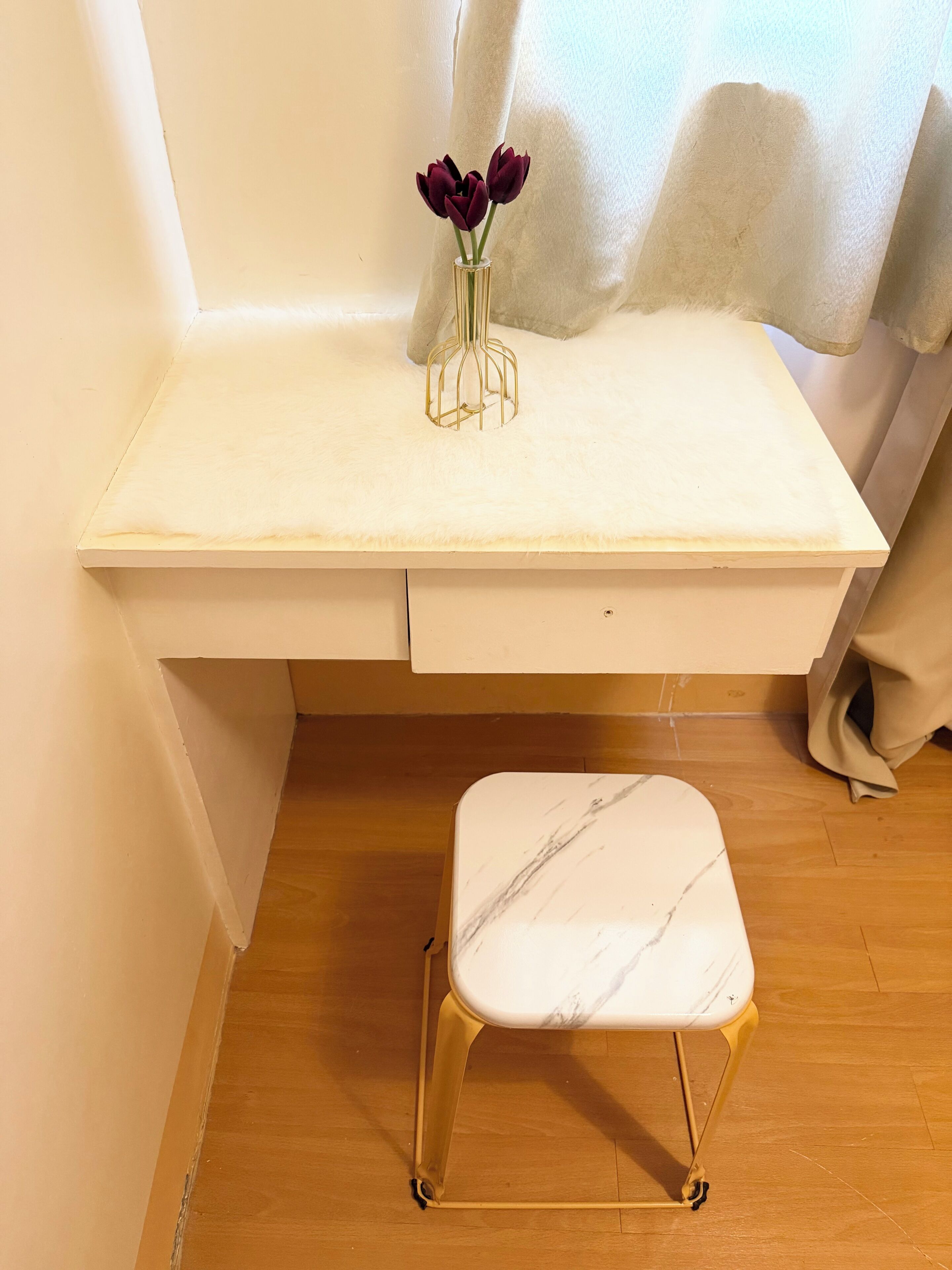 Un petit bureau blanc, orné d’un vase de fleurs violettes, et une chaise blanche aux pieds dorés.