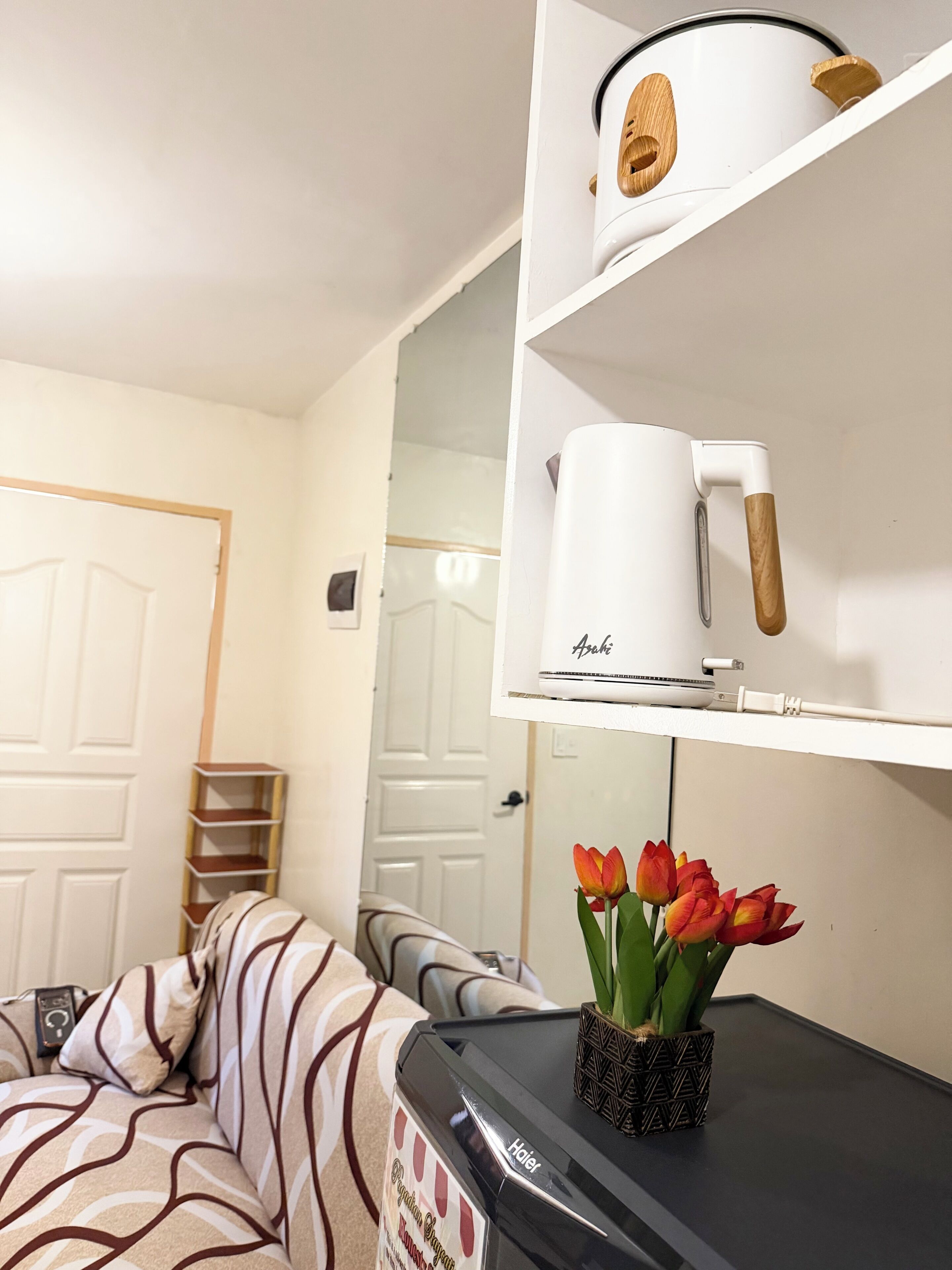 Ein Zimmer mit einer Couch, einer Kaffeemaschine, einem Wasserkocher und einer Vase mit Tulpen.